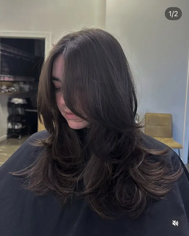 Dark brunette layered haircut with curtain bangs and a polished salon finish.